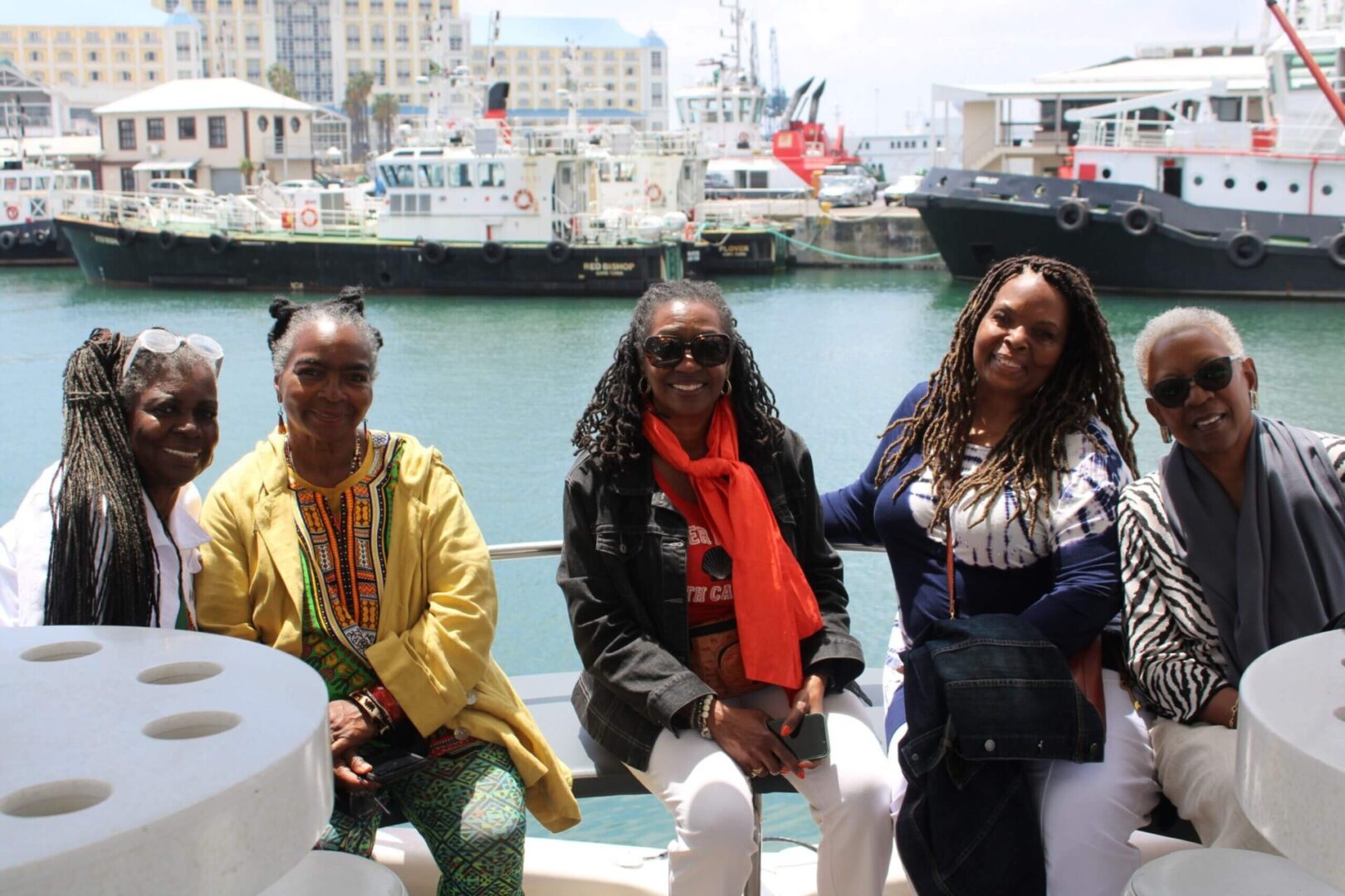Three women sitting on a boat in front of some boats.