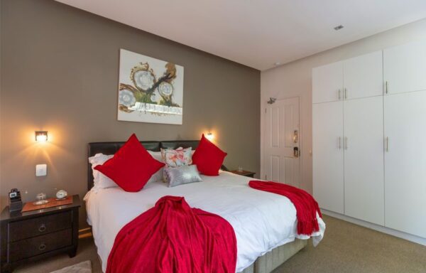 A bedroom with a bed, pillows and red sheets.