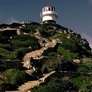 A lighthouse on top of a hill with people walking up the steps.