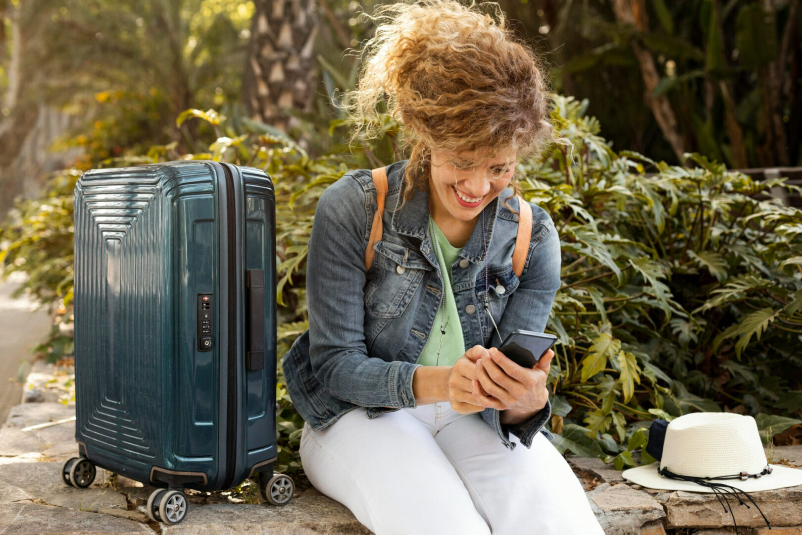 A woman sitting on the ground with her luggage looking at her phone.
