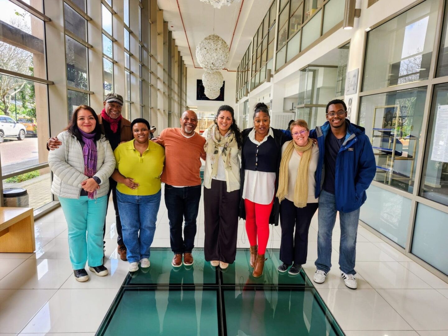 Group of seven casually dressed adults posing indoors in a bright modern building.