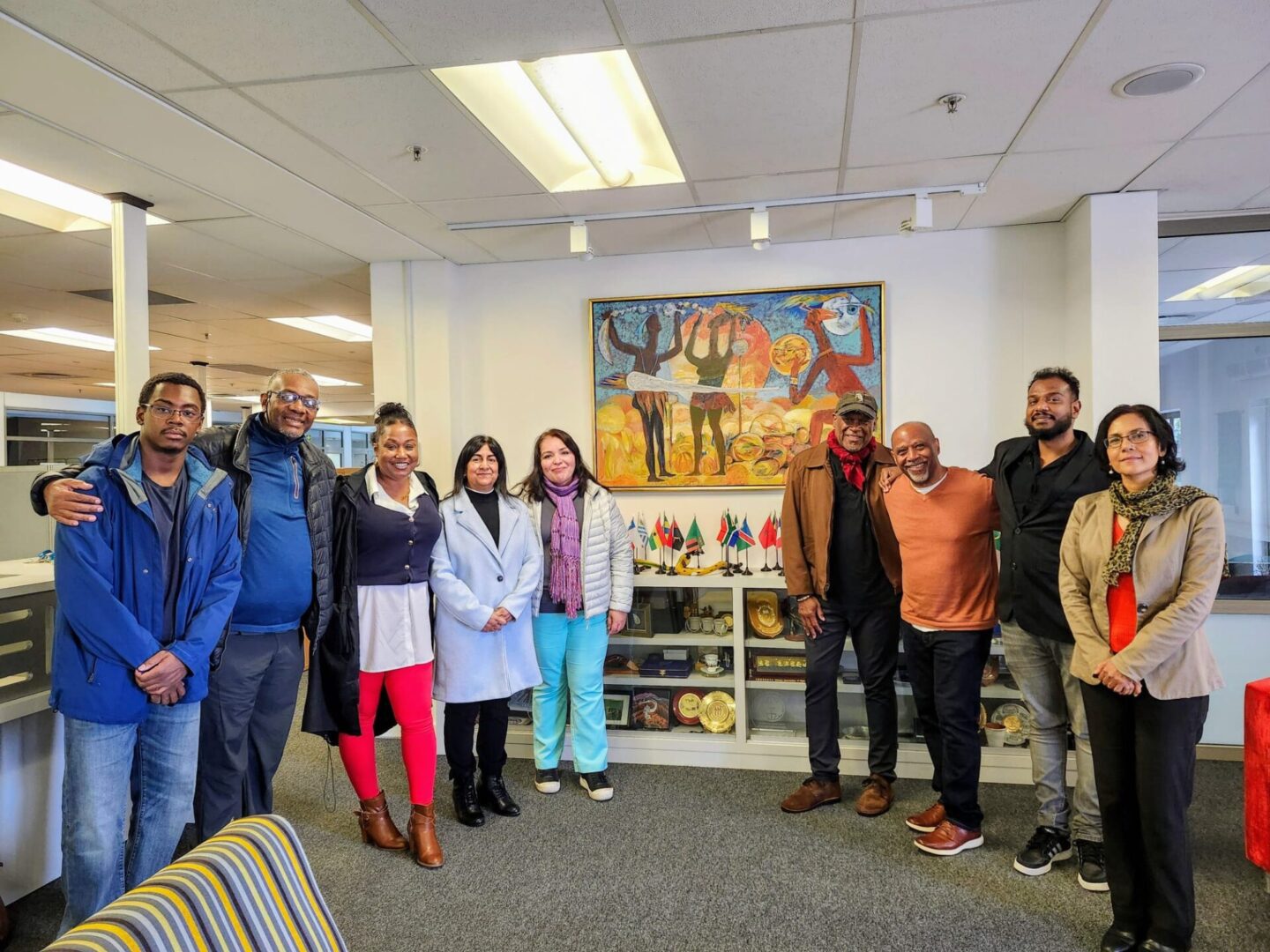 A diverse group of people posing in an office with colorful art on the wall.